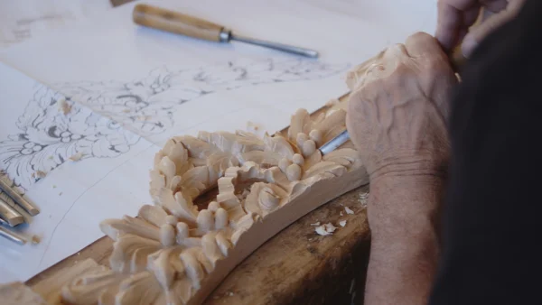 Master carving an ornate floral wood relief from a design drawing