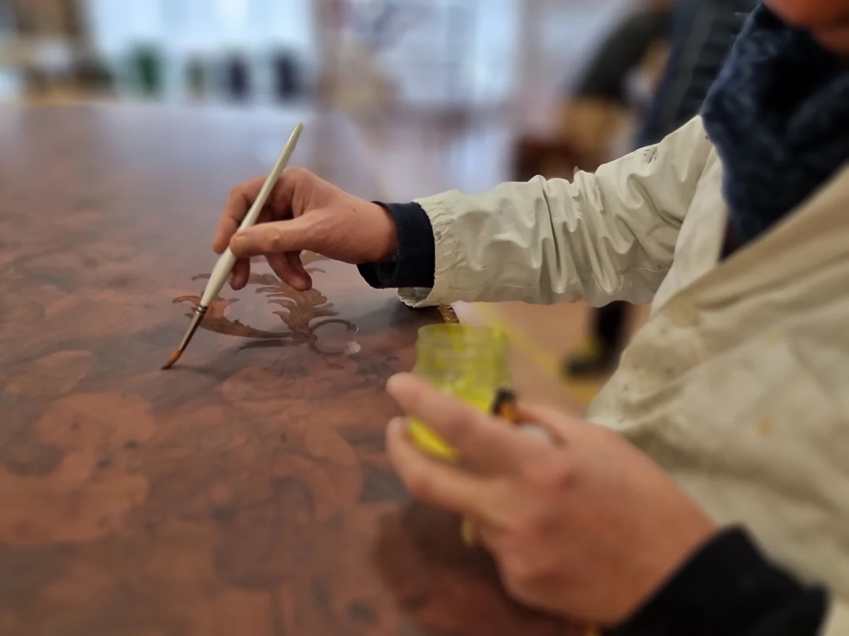 Artisan applying finish to a burl-wood tabletop in the Modenese workshop