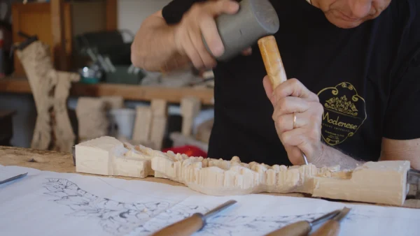 Italian master carving a decorative wood element with mallet and chisel