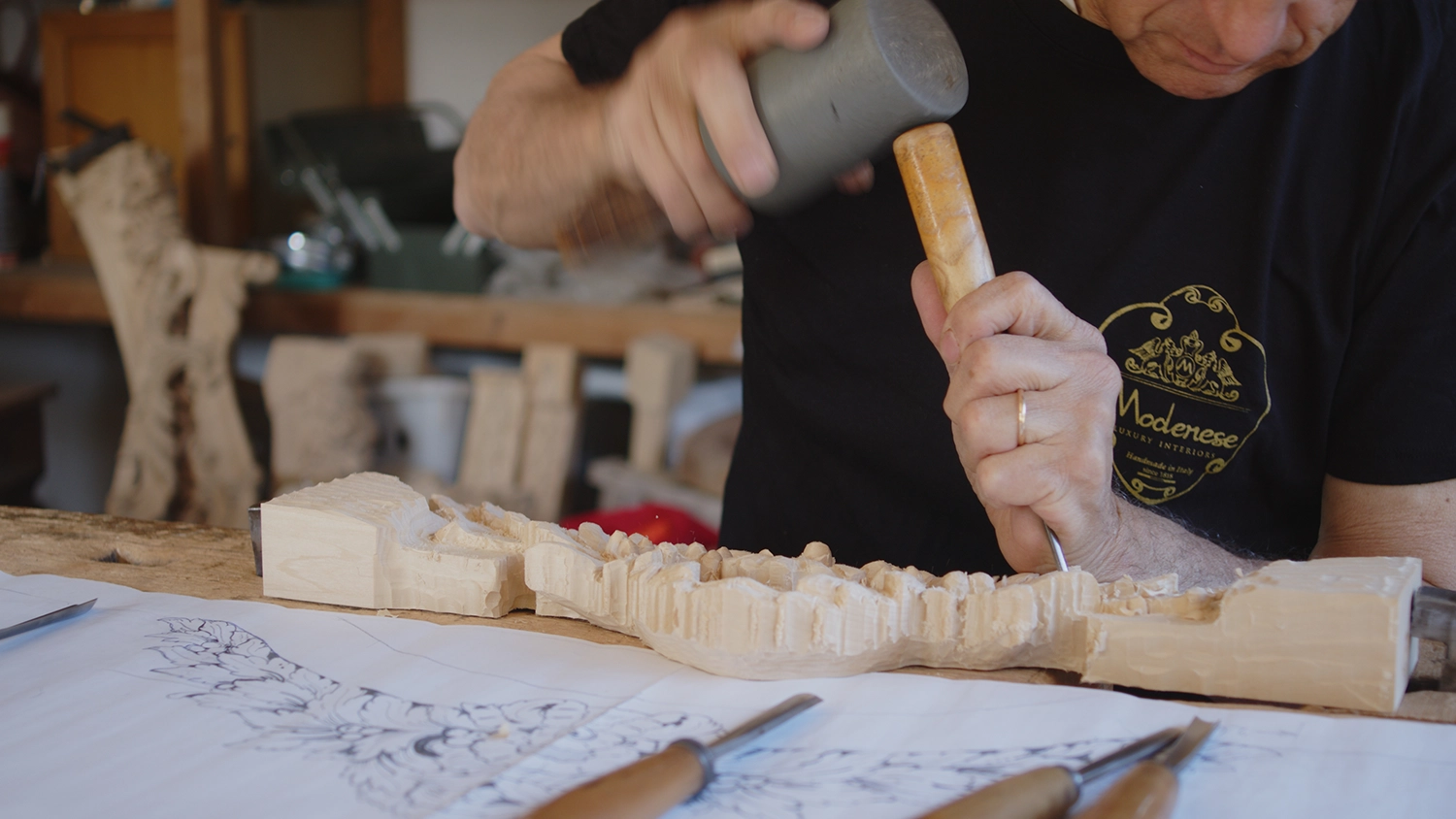 Italian master carving a decorative wood element with mallet and chisel
