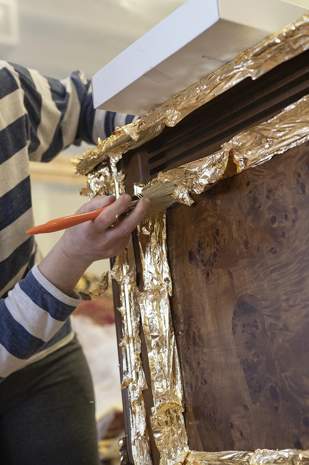 Master craftsman applying gold leaf to a carved wood frame