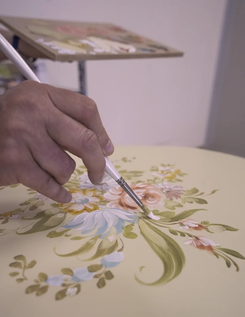 Artisan hand-painting a floral motif on ivory lacquered الأثاث